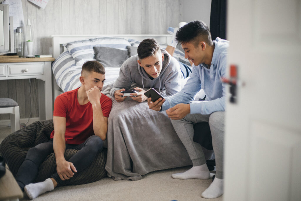 Tre drenge slapper af i et værelse. En af drengene viser de to andre noget på sin telefon.
