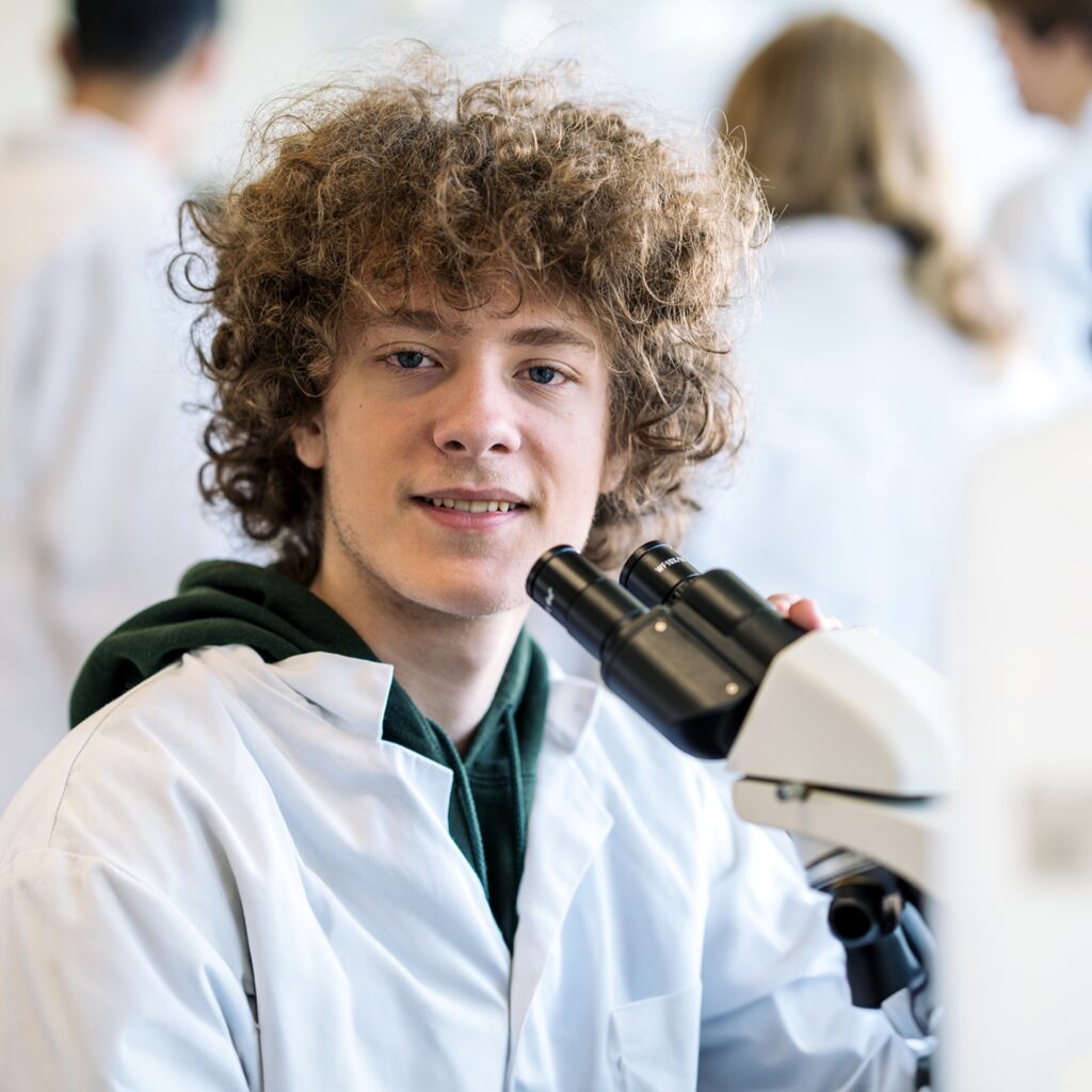 En elev fra NEG Kalundborg sidder iført kittel og har et mikroskop foran sig.