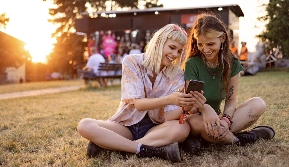 To piger sidder på græsset og kigger på noget på den enes telefon.