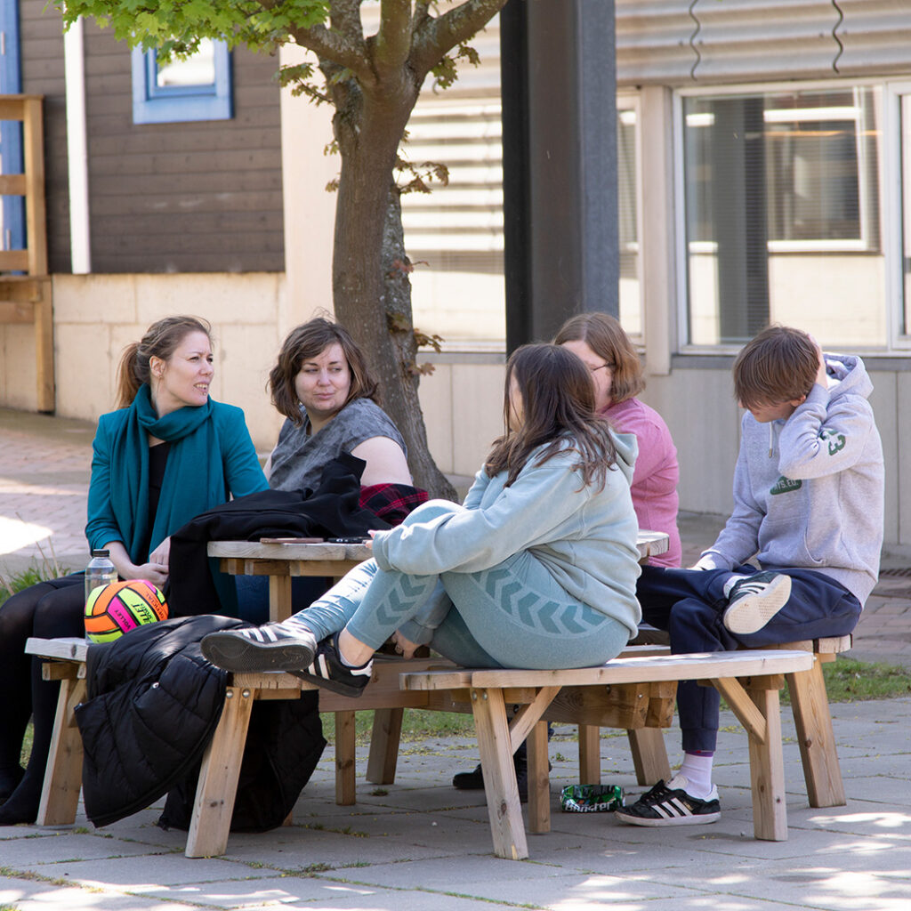 Fem elever fra NEG Kalundborg sidder udenfor sammen. De sidder ved et borde bænkesæt.